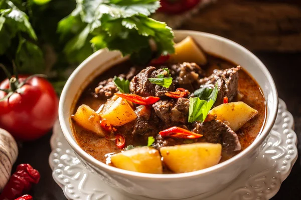 Bowl of goulash with meat, potatoes, chillies and parsley.