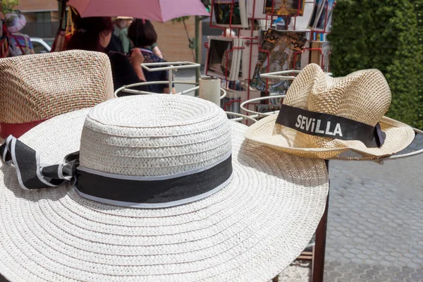 A straw woman\'s hat with ribbon and a straw man\'s hat with the inscription Sevilla. Summer goods for tourists in Spain in a tourist place