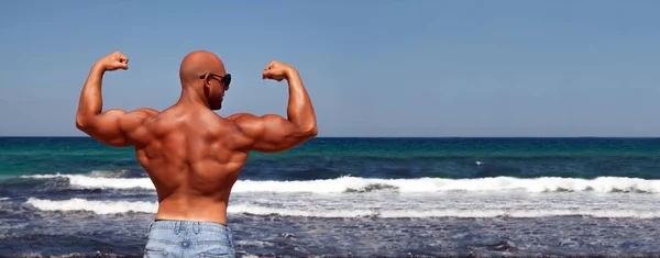 Açık spor ve sağlıklı yaşam afiş. Pazı ve omuz mavi deniz ve gökyüzü karşı göstermek için silah esneme ile poz İtalyan vücut geliştiricisi. Geniş panorama