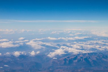 Güzel mavi gökyüzü beyaz dokusal bulutlar ve güneşli gün dağlarda, uçak penceresinden görüntülemek