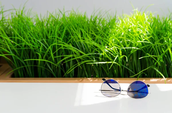 Parlak yeşil çim zemin üzerine beyaz masada moda mavi güneş gözlüğü.