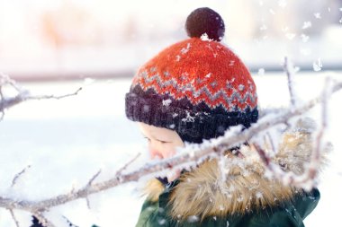 Parlak turuncu şapkalı bir çocuk karlı kış parkı boyunca yürüyor