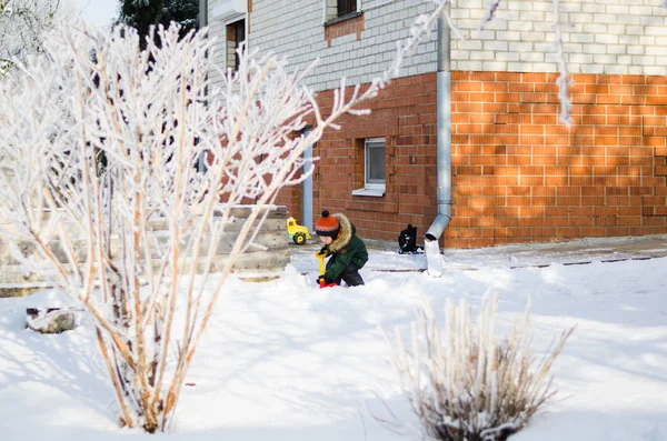 Kleiner Junge spielt im Winter mit Schneeschaufel im Hof lizenzfreie Stockbilder