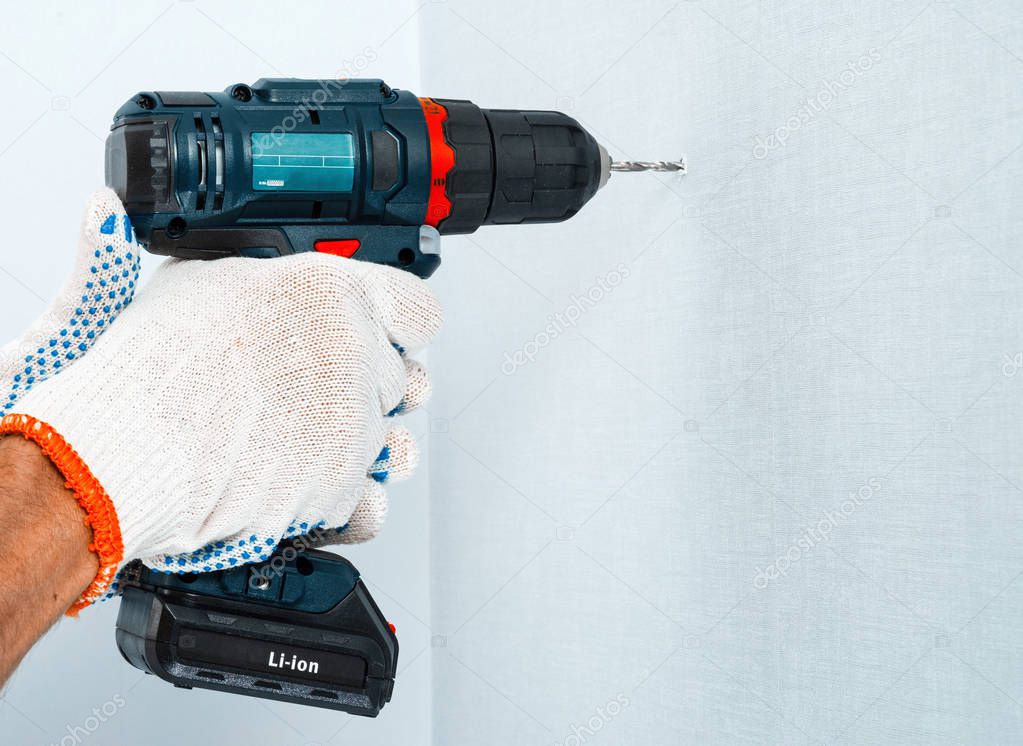 Drilling the wall with a cordless drill in protective gloves.