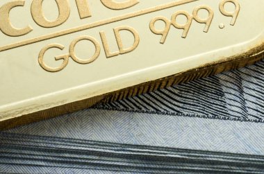 Yüz dolarlık banknotlar bir yığın üzerinde basılan altın bar yatıyor.