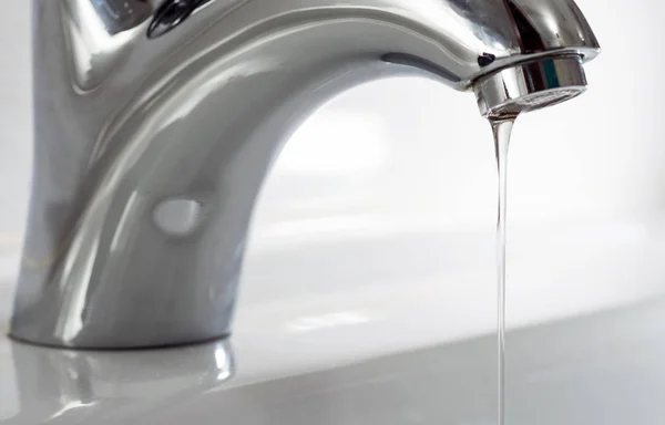 A thin trickle of clean water pours from the tap into the sink.