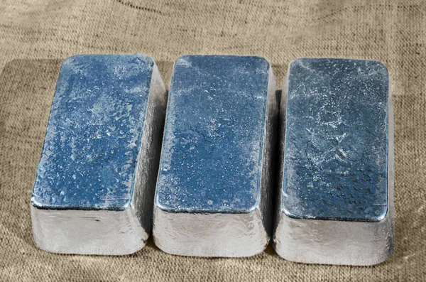 Three unmarked silver bars against a rough textile texture. Selective focus.