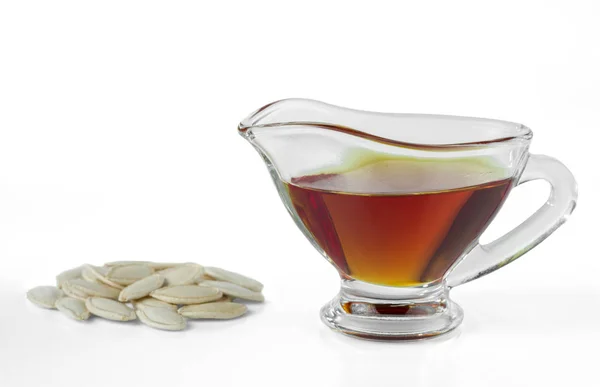 Pumpkin oil in a glass gravy boat and pumpkin seeds isolated on white background.