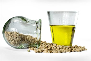 Kenevir tohumu yuvarlak cam kavanoz ve hempseed petrol beyaz bir arka plan üzerinde izole bir ölçüm cam ölçek.