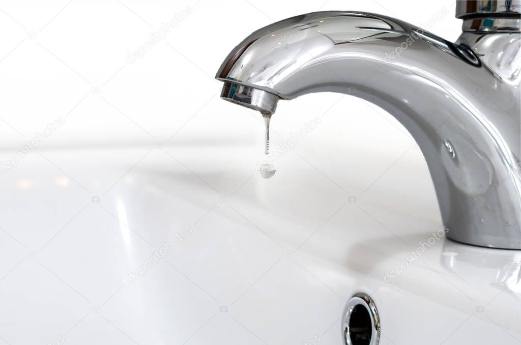 Faucet with a drop of water against a white sink. Water leaking and saving.