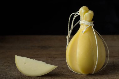 Tipik İtalyan peynir Caciocavallo bir ahşap yüzeyde. Baş ve dilim peynir karanlık bir arka plan üzerinde