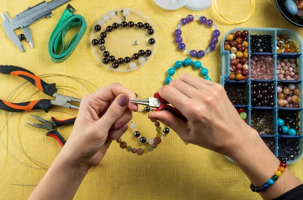 Jewelry making. Female hands with a tool on a yellow background