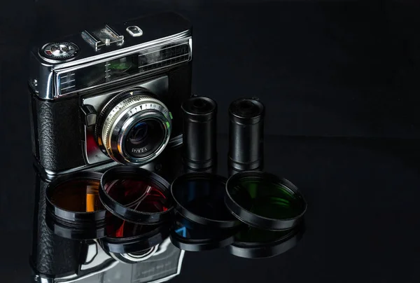 Vintage film camera, film cassettes and color filters on a dark background.