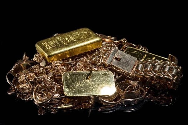 A pile of gold bars and gold jewelry on the black background. Selective focus.