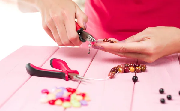 Jewelry making. Female hands with a tool on a pink table. Selective focus