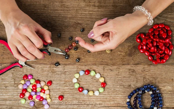 Making bracelet of colorful beads. Female hands with a tool on a rough wooden table.