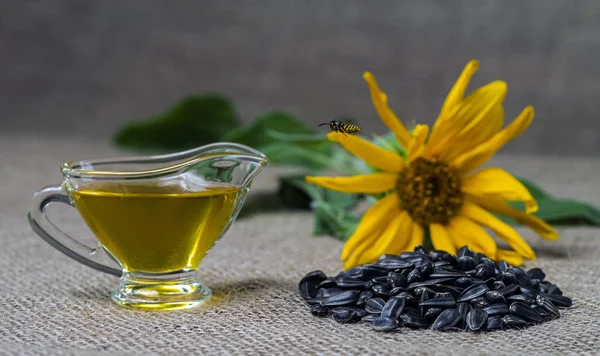 Sunflower oil in a glass gravy boat and a handful of sunflower seeds on the background of burlap and sunflower. Flying wasp.
