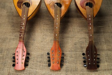 Üç yaşlı mandolinler kaba burlap doku bir arka plan üzerinde kameraya fingerboards döndürülmüş. 