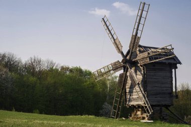 Wooden windmill and millstone on the hillside against a background of forest and blue sky. Selective focus.