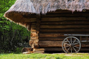 Sazdan çatı altında bir günlük evin arka planına karşı ahşap tekerlekler ile eski sepeti.