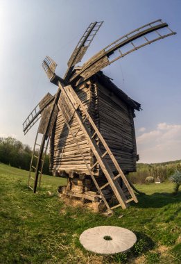 Wooden windmill and millstone on the hillside against the backdrop of the rural landscape. Selective focus.