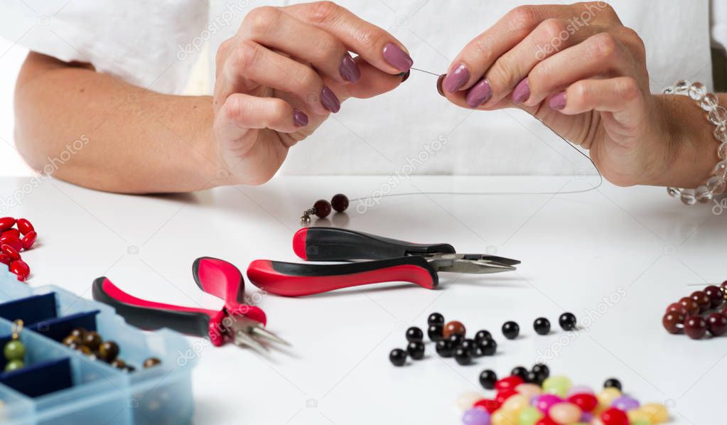Jewelry making. Making bracelet of colorful beads. Female hands with a tool. Selective focus