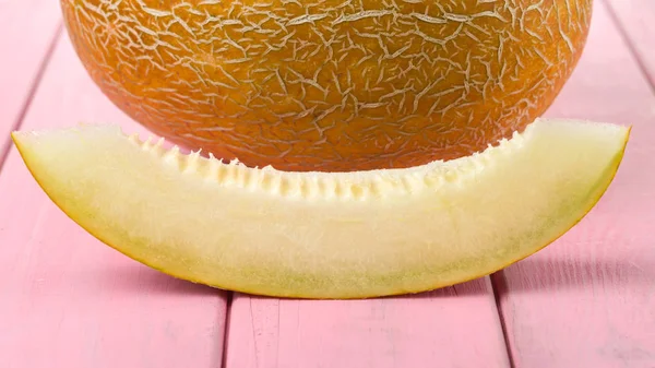 A piece of melon and a whole melon on a pink painted background.