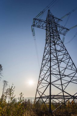 Mavi gökyüzüne ve parlak güneşe karşı yüksek voltajlı elektrik hattı.