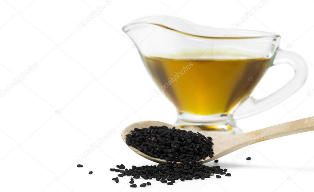 Black cumin seeds on a wooden spoon on a background of a glass gravy boat with black seed oil. Selective focus. Isolated on white.