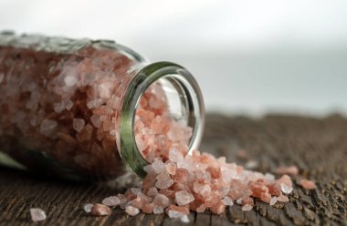 Pembe Himalaya tuzu kristalleri kaba ahşap bir yüzeyde cam bir şişenin yanında. Seçici odak.