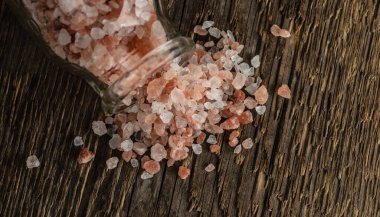 Pembe Himalaya tuzu kristalleri kaba ahşap bir yüzeyde cam bir şişenin yanında. Seçici odak.