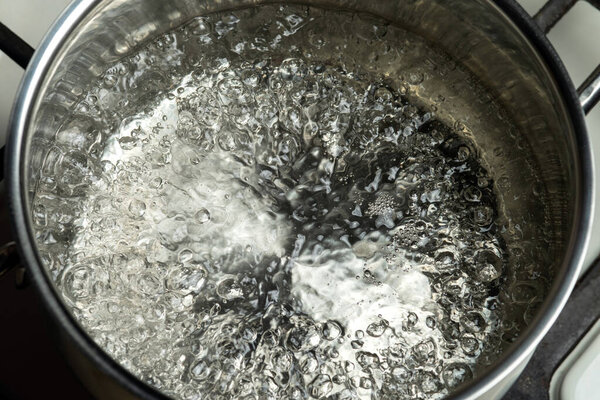 Water boils in a stainless steel pot. Boiling water surface.