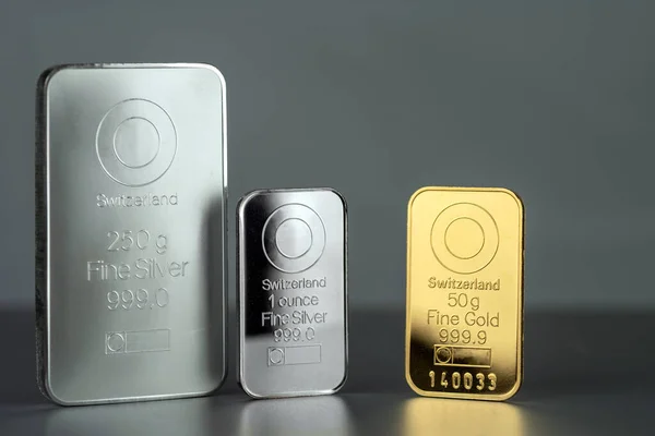 Gold and silver bars of different weight on a gray background.