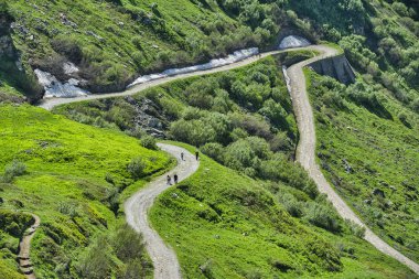 dağ tepeleri ve bahar mevsiminde güneş ışınları tarafından aydınlatılmış çim ile toprak yol üzerinde yürüyen insanlar