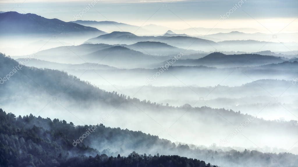 Foggy landscape on the hills in a winter cold morning seen from the mountains near the city of Varese