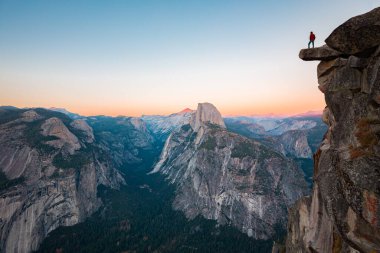 Korkusuz bir yürüyüşçü güzel akşam alacakaranlık, Yosemite Ulusal Parkı, Kaliforniya, ABD'de güzel akşam alacakaranlık bakan Glacier Point ünlü Yarım Kubbe doğru manzarasının keyfini sarkan bir kaya üzerinde duruyor