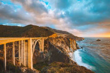 Yaz aylarında dramatik bulutlu bir gün batımında güzel altın akşam ışık dünyaca ünlü Highway 1 boyunca tarihi Bixby Creek Köprüsü Manzara panoramik görünümü, Monterey County, California, Abd
