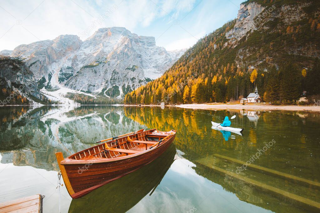 Beautiful view of famous Lago di Braies with traditonal rowing boat and young man in kayak at sunrise in fall, Dolomites, Italy