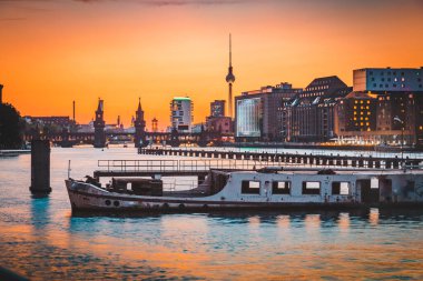 Alacakaranlıkta Spree Nehri'nde yatan eski gemi enkazı ile ünlü Tv kulesi ve Oberbaum Köprüsü ile Berlin siluetinin panoramik görünümü, Berlin Friedrichshain-Kreuzberg, Almanya.