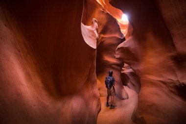 Amazing sandstone formations with male hiker looking at light beam in famous Antelope Canyon on a sunny day near the old town of Page at Lake Powell, American Southwest, Arizona, USA clipart