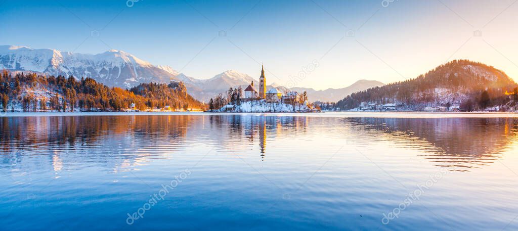 Beautiful view of famous Bled Island (Blejski otok) at scenic Lake Bled with Bled Castle (Blejski grad) and Julian Alps in the background in golden morning light at sunrise in winter, Slovenia.