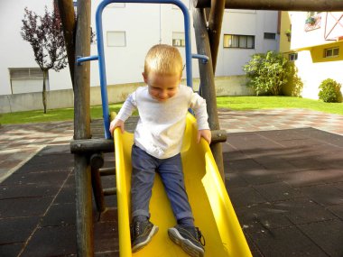     Parkta sarı plastik bir kaydırak süren üç yaşındaki yakışıklı bir çocuk..                                                         