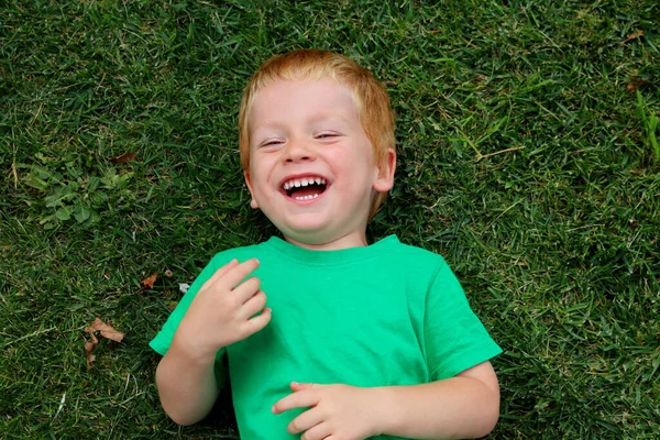 Blond Pojke Ligger Det Gröna Gräset Och Smalnar Sina Ögon — Stockfoto