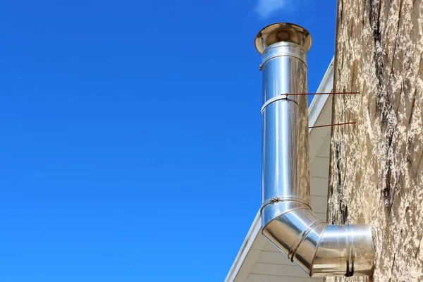 Bir evin üst katındaki gaz kazanından mavi gökyüzüne karşı hava ve gaz sağlamak için paslanmaz çelik havalandırma borusu. Kavram: Isıtma sistemini soğuk mevsime hazırlamak.