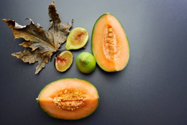 Olgun ve sulu bir kavun dilimi ve gri arka planda tatlı incirler. Sonbahar, kavun ve incirle dolu bir hayattır. Sonbahar meyveleri.