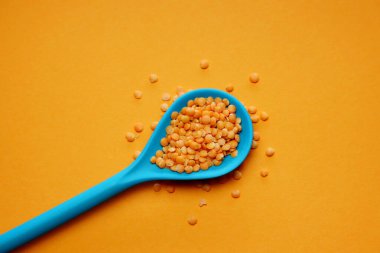 Turuncu arka planda mavi bambu kaşıkta kırmızı mercimek..