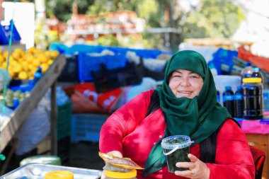 Aikiricay, Türkiye-Nisan 1, 2015: onun imtiyaz ahır D-635 yol veya Elmalı-Finike Yolu Arykanda Harabeleri yürüyerek geçen yeşil hijab-headdress satıyor zeytin-meyve-petrol giyen pazarlamacı.