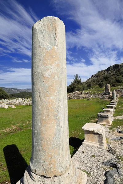 Ruins of the agora. Standing column at its S.E.corner and the Inscribed Obelisk on background -inscribed monolith in Ancient Greek-Lycian-Mylian languages dated 425-400 BC.- of Xanthos-Lycia-Turkey.