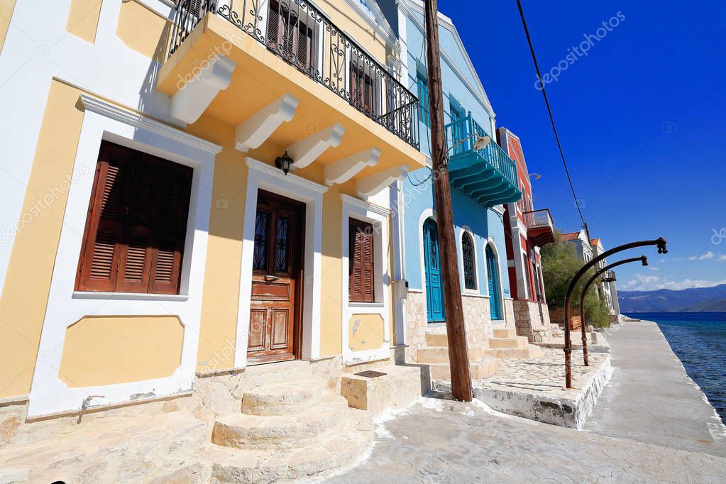 Restored neoclassic two-story port-facing houses with balconies painted yellow-blue-maroon on the Pera Meria district-west side of the main harbor. Kastellorizo island-Dodecanese-Rhodes reg.-Greece.