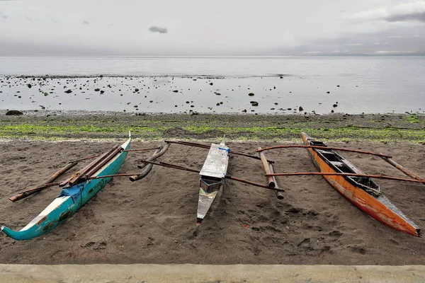 Geleneksel Filipinli bangka usülü balıkçı tekneleri, Rizal Bulvarı boyunca, alçak gelgitte Bohol Denizi 'ne bakan yağmur sahili boyunca karanlık kumda karaya oturdu. Dumaguete-Zenciler Doğu-Merkez Visayas-Filipinler
